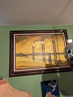 Mid-century original bridge painting hanging on a green wall, showing the full framed artwork with a lamp and other room elements partially visible.