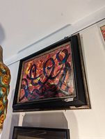 Framed original abstract painting with fluid brushstrokes in multiple colors, mounted on a white wall.