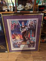Framed Flash Gordon movie poster with colorful scenes and signed by actor, displayed leaning against a wooden surface.
