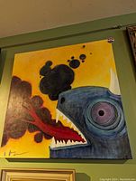 Photo showing a colorful and surreal original painting of a blue horned creature breathing fire against a yellow background, signed by the artist.