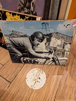 Photo of original racing-themed artwork titled 'Racer' showing a motorcyclist with helmet and racing suit on a bike, industrial background, 18x24 inch size