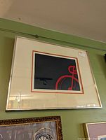 Framed signed abstract bike print hanging on green wall showing corner and overall framing.