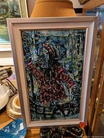 Framed abstract painting with rich textures and mixed dark colors, predominately blues and reds, displayed upright indoors.