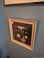 Photo of framed black and white abstract face print measuring 12x12 inches hanging on wall.