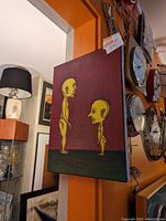Photo of a small original painting on canvas showing two strange stylized humanoid figures against a maroon background with dark green ground.