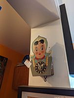 Photo showing the front view of the doll-shaped strange clock with painted bonnet and face. Clock face is on the torso with a non-functioning clock mechanism.