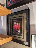 Photo showing framed artwork with three women in bright red and blue dresses, multi-layer matting, glass-covered, measuring approximately 13x16 inches.
