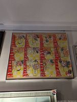 Framed colorful abstract painting in nine panels with human faces and floral themes, hanging on a wall