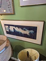 Wide horse serigraph artwork hanging on a green wall above lampshades, showing the framed print with horse images in multiple motion overlapping.