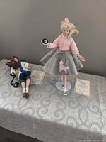 Both Peggy Sue and Patty Joe dolls displayed standing and laying down with certificates on patterned cloth surface