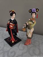 Two Asian figurines, one in black kimono and one in white/green robe, photographed on table