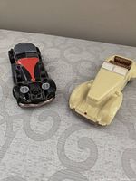 Top view of two Avon collectible cars, one black and red with fabric roof and one cream convertible.