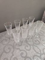 8 crystal champagne flutes arranged in two rows on a patterned tablecloth, showing the intricate cut design and faceted stems