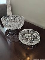 Two clear crystal items on dark wood surface: deep bowl and ashtray with pinwheel pattern.