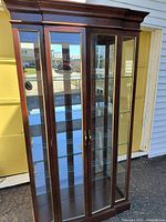 Front-facing view of dark cherry wood curio cabinet with glass doors and brass-tone handles