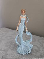 Front view showing Princess Diana figurine wearing a light blue, strapless gown with a flowing scarf wrapped around her arms and trailing behind.