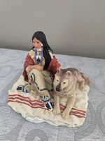 Front angle view of the painted ceramic figurine featuring a young Indigenous woman and wolf on a blanket
