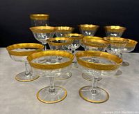 Set of 14 vintage liquor glasses arranged on a table, showing the gold rimmed detail and shape variety.