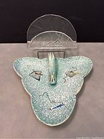 Top view of turquoise ceramic atomic birdcage tidbit plate with clear glass napkin holder behind it on display surface