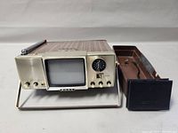 Front view of the Sony micro-TV showing the small CRT screen, tuning dial, controls, woodgrain casing, and metal foldable stand.