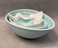 Nested light blue egg-shaped stoneware bowls stacked with paper towels inside