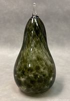 Front view of the signed vintage art glass pear paperweight showing mottled green coloration and clear glass stem on top.