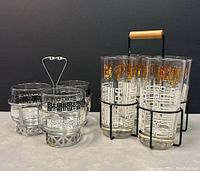 Photo of both sets of vintage drinking glasses with respective metal caddies on a neutral background.