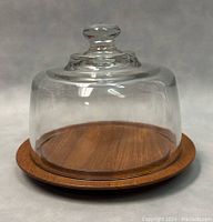 Front view showing teak wood base with smooth finish and grain, and clear glass dome lid with knob handle on top.