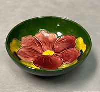 Front angled close-up of the bowl showing the red anemone flower detailed with yellow center and surrounding yellow leaves on a green background.