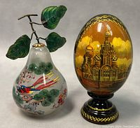 Front and side view of the Chinese inside hand painted glass pear with enamelled leaves and the Russian lacquered hand painted egg featuring a cathedral scene on black lacquered base.