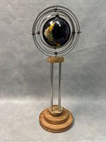 Full view of the vintage world globe mounted in metal concentric rings on a wooden base with three vertical metal supports.