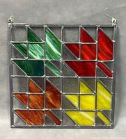 Front view of stained glass panel against gray background showing green, red, orange, yellow colored glass pieces segmented by lead framing.