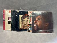 Photo showing seven vinyl LP records in their sleeves, some with visible artist names and portraits, including Leonard Cohen album at center.