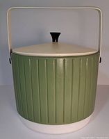 Front view of vintage avocado green insulated ice bucket with white lid and black knob, ribbed textured exterior and metal handle.