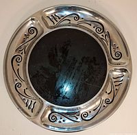 Top view of round cheese board showing black marble center and silver metal rim with intricate black swirled decorative patterns and six sectioned compartments