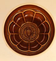 Top view of the brown glazed ceramic jello mold showing interior with acorn and wreath design in center and scalloped edges.