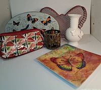 Full display of the lot items including the make-up bag, butterfly tin, candle holder, vase, wire decor, and plate.