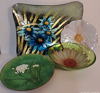 All four decorative flower plates in metal, glass, and plastic arranged together