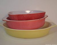 Stacked view of three Pyrex dishes: large yellow oval dish on bottom, pink round dish in middle, red hostess bowl on top.