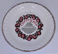 Top view of pie plate showing cherry wreath graphic and cherry pie recipe text in the center with brown striped edge pattern.