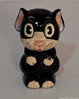 Front view of the black cat-shaped ceramic perfume bottle showing facial features and painted details.