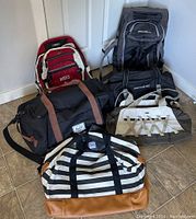 Photo showing six bags including a black Herschel duffle with brown accents, black Samsonite duffle, red Roots backpack, Eddie Bauer black rolling duffel, Columbia striped duffle, and a black and grey duffle.