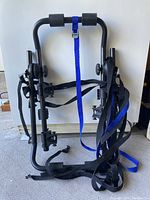 Full view of folded black metal portable bike rack showing attached straps for mounting and securing bike.