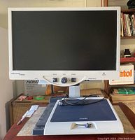 Front view showing the monitor sitting above the black magnification platen, with control panel under the screen and power cable on platen.
