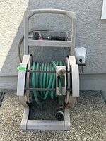 Front view of Suncast hose reel with attached green garden hose coiled and multi-function spray nozzle on top shelf.