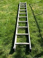 Full view of aluminum ladder lying on grass, showing non-slip rubber feet and even spacing of rungs.