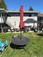 Outdoor round metal table with red umbrella in closed position in grassy yard, photographed from different angles to show condition and measurements.