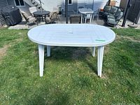 View of the white plastic outdoor table from one side showing oval shape and four legs on grass.