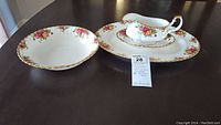 Photo of the 9.5 inch serving bowl and 15 inch platter with floral rose pattern and gold trim on dark table