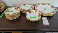 Multiple stacks of Royal Albert Old Country Roses plates and bowls arranged on a wooden surface, showing variety of sizes and pattern details.